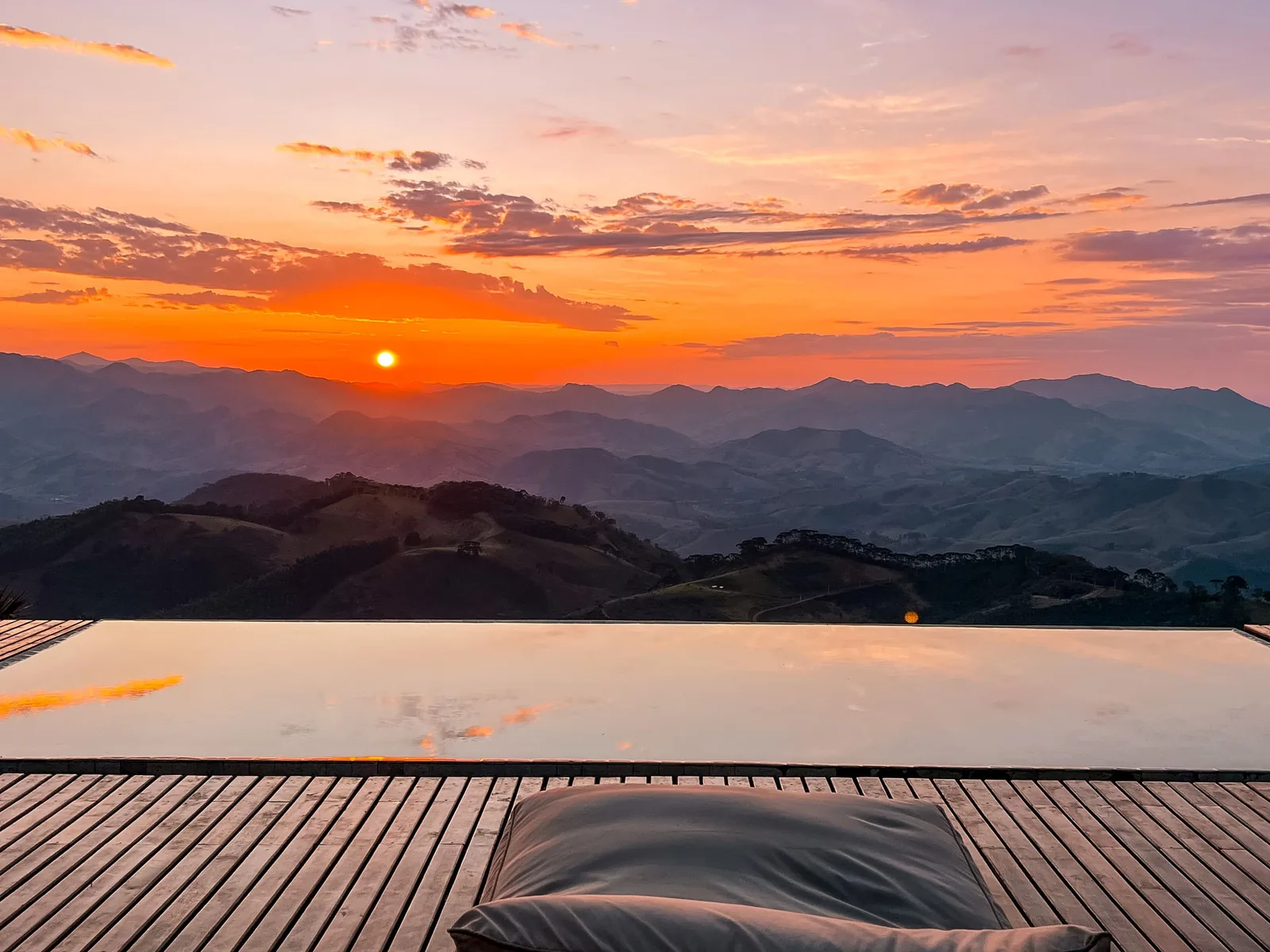 Pôr do sol intenso em laranja e rosa sobre as montanhas, refletido na piscina e no deck