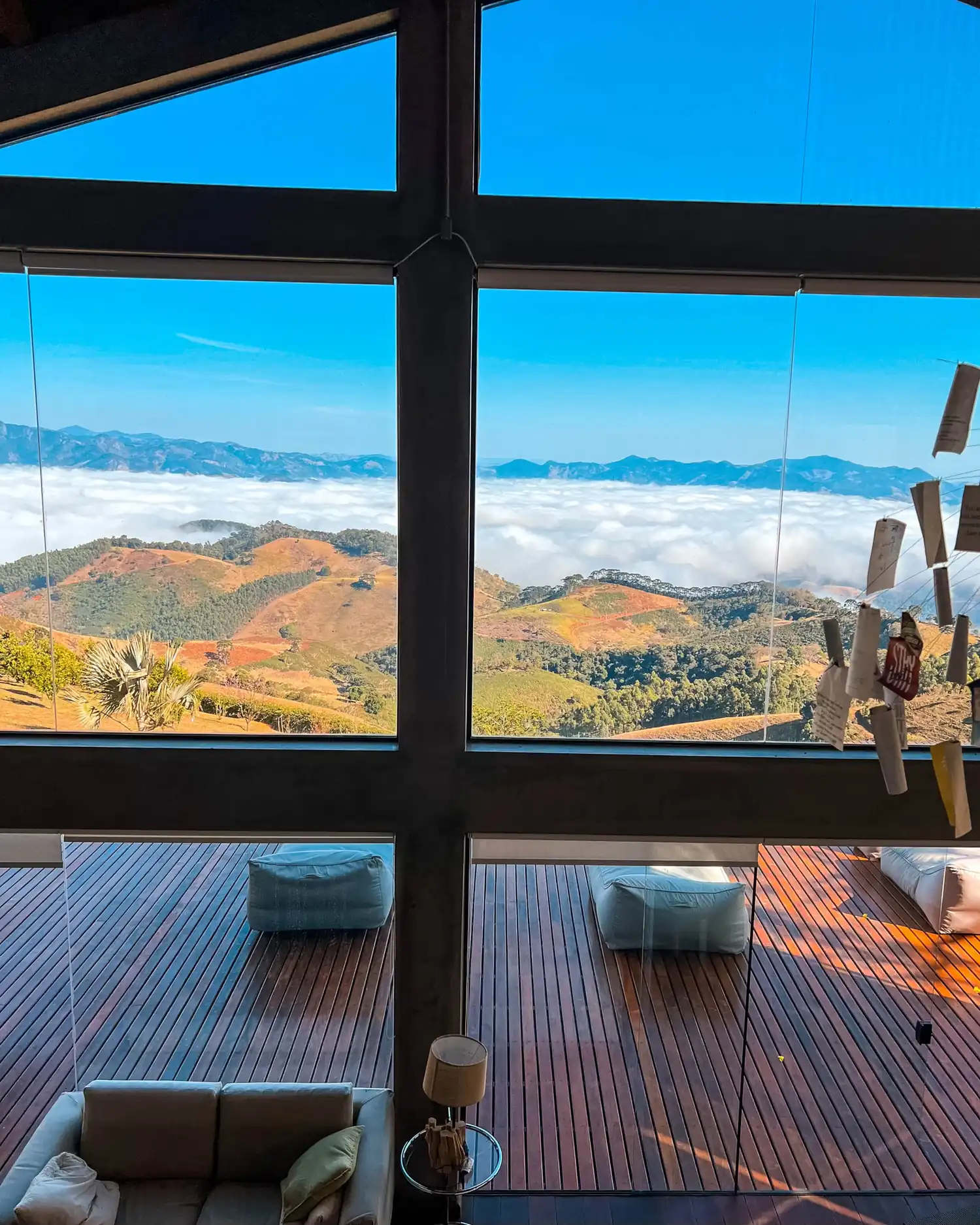 Sala de estar com paredes de vidro do piso ao teto, abrindo para o mar de nuvens e o deck de madeira